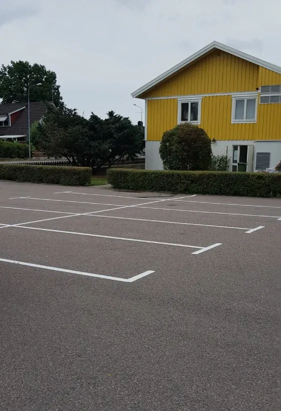 Vita parkeringsrutor på asfalt framför ett gult hus